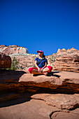 Junge kaukasische Frau sitzt mit gekreuzten Beinen auf dem Canyon Overlook Trail im Zion National Park, Utah