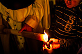 A Nazareno assists a young child in making a wax ball during Holy Week in Seville, highlighting a cherished local tradition.