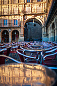 Cafe-Tische auf der Plaza Mayor von Salamanca, in denen sich das Morgenlicht und architektonische Details spiegeln.