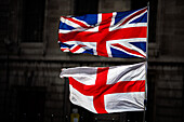 Union Jack and Saint George's Cross flags displayed outdoors against a historic building.