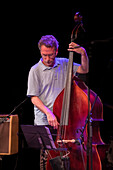 Jazz musician Larry Grenadier performing with a double bass in an intimate indoor setting.
