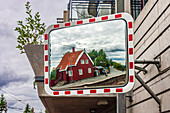 A reflective mirror at a commuter station captures a charming red house and the surrounding landscape in Oslo, Norway on a cloudy day.