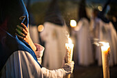 A nighttime procession featuring penitents with traditional outfits holding candles during Holy Week.