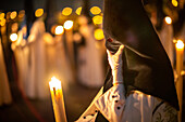 A nighttime procession featuring penitents with traditional outfits holding candles during Holy Week.