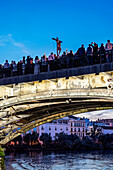 Worshippers admire El Cristo del Cachorro as it shines above Triana Bridge, creating a stunning reflection in the river at dusk.