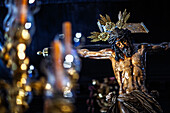 The crucified figure of the Hermandad del Amor is illuminated by candlelight, showcasing intricate details during Holy Week in Seville.