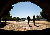 Silhouetted pedestrians walking through Triana Bridge arch towards Muelle de la Sal in Seville.