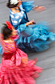 Flowing figures of women in colorful flamenco dresses move gracefully toward the Feria in Seville, captured with long exposure for motion.