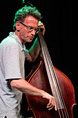 Jazz musician Larry Grenadier performing with a double bass in an intimate indoor setting.