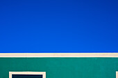 Grüne Gebäudefassade im Kontrast zu einem strahlend blauen Himmel und weißen Rändern.