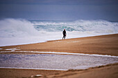 Man walking on Praia do Norte (North Beach), listed on the Guinness World Records for the biggest waves ever surfed, formed under the influence of the Nazare Canyon, Portugal