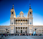 Frontansicht der Fassade der Almudena-Kathedrale bei klarem Himmel mit einer Menschenmenge in Madrid.