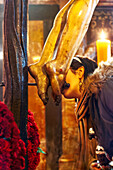 A girl kisses the feet of Cristo del Calvario at Magdalena church, honoring the religious tradition during a solemn moment in Seville.