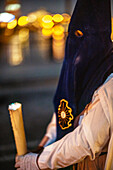 A nighttime procession featuring penitents with traditional outfits holding candles during Holy Week.