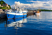 Boote liegen friedlich am Aker Brygge Dock in Oslo unter einem strahlend blauen Himmel und flauschigen Wolken, die sich auf dem ruhigen Wasser spiegeln.