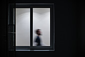 Silhouettierte Person in Bewegung, gesehen durch ein beleuchtetes Fenster bei Nacht.