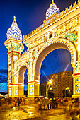Seville, Spain, May 9 2014, The vibrant gateway of the Seville Fair shines brightly at twilight, drawing crowds to enjoy the festive atmosphere and activities.