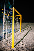Yellow soccer goalpost on a sandy beach under night lighting in Barbate, Spain.