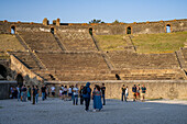 Tourists in the arena of the Amphitheater of Pompeii in the ancient Roman ruins of Pompeii in Italy.