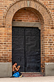 A homeless man sits by a door of the Metropolitan Cathedral of Medellín in Medellin, Colombia.