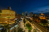 Evening twilight in Medellin, Colombia, with the Palace of Culture at right. A long exposure produces streaking lights from vehicles and a train.