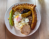 A traditional Bandeja Paisa or Colombian Plate in a roadside restaurant in Colombia. Beans, rice, ground beef, pork sausage, blood sausage, fried pork belly, fried egg, ripe plantain, salad, avocado and an arepa.