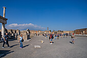 Tourists in the Forum or Foro Civil in the ancient Roman ruins of Pompeii, Italy. Mt. Vesuvius is behind.