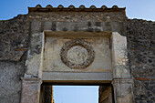 Carved wreath over the doorway of the House of Augustalis, Building II.2.4, in the ancient Roman ruins of Pompeii, Italy.