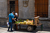 A man buying produce from a street vendor with a mobile cart in Rionegro, Colombia.