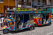 Eine Reihe farbenfroher Motochivas oder Mototaxis, touristische Verkehrsmittel in der Stadt Guatape, Kolumbien.