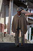 Old man walking with a hat and ruana.