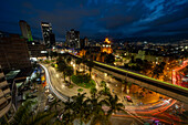 Evening twilight in Medellin, Colombia, with the Palace of Culture at center. A long exposure produces streaking lights from vehicles and a train.