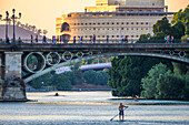 Ein junger Mann übt sich im Paddelsurfen auf dem Fluss Guadalquivir neben der Triana-Brücke und fängt damit die Essenz des pulsierenden Lebens in Sevilla ein.