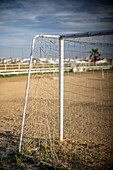 Ein Torpfosten steht auf einem unbefestigten Fußballplatz in Carrión de los Céspedes, Sevilla. Die ländliche Umgebung bietet eine ruhige, malerische Kulisse für das Spiel.