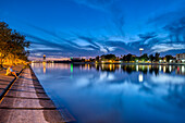 Die Farben des Sonnenuntergangs spiegeln sich im Guadalquivir-Fluss wider und lassen die Insel La Cartuja, die Barqueta-Brücke und den Torre Sevilla in einem ruhigen Abendlicht erscheinen.