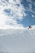 Active woman running and jumping mid-air on white snow hill against sky