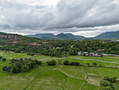 Luftaufnahme von üppig grünem Ackerland und ruhigen Bergen unter einem bewölkten Himmel, Nui To, Tri Ton, An Giang, Vietnam.