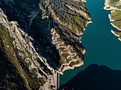Aerial view of serene Bovilla Lake surrounded by picturesque mountains and a winding road through lush greenery, Herraj, Tirana, Albania.