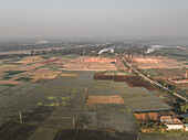Luftaufnahme von Ziegelfeldern und einer Fabrik inmitten von grünem Ackerland mit Rauch, Paikar Char, Narsingdi, Dhaka, Bangladesch.