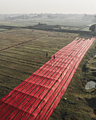Aerial view of a colorful cloth factory with people drying fabric in a rural landscape, Paikar Char, Narsingdi, Dhaka, Bangladesh.