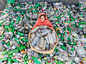 Narayanganj, Bangladesh - 09 November 2024: Aerial view of a woman worker sorting plastic bottles at a recycling center amidst a polluted landfill, Narayanganj, Dhaka, Bangladesh.