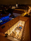 Aerial view of a festive advent market with illuminated buildings and a historic church in a bustling square, Zagreb, Croatia.