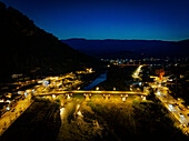 Aerial view of illuminated Gorica Bridge over the river with a scenic cityscape and mountains at twilight, Mangalem, Berat, Albania.