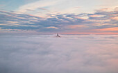 Luftaufnahme des majestätischen Mont Saint-Michel, umgeben von weichen Wolken und einem malerischen Himmel bei Sonnenuntergang, Le Mont-Saint-Michel, Manche, Frankreich.