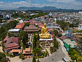 Luftaufnahme einer goldenen Buddha-Statue und eines Tempels inmitten einer friedlichen, von Bergen und Bäumen umgebenen Stadtlandschaft, Ward 8, Da Lat, Lam Dong, Vietnam.