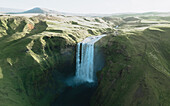 Aerial view of the majestic Skogafoss waterfall cascading down a rugged cliff surrounded by lush green grassland, Skogafoss, Iceland.