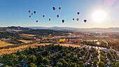 Aerial view of colorful hot air balloons floating over a scenic valley with mountains and cityscape, Reno, Nevada, United States.