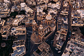 Aerial view of rotunda St. John Baptist Church amidst historic stone buildings and rooftops, Dingli, Malta.