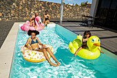 Eine fröhliche Familie genießt einen sonnigen Tag in einem Pool und entspannt sich auf aufblasbaren Schwimmern. Der Fokus liegt auf Spaß und Zusammensein in einer schönen Umgebung im Freien.