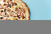 Top view of a gourmet pizza with roast duck fillet, figs, almonds and truffle sauce, beautifully presented on a pastel blue background that adds a touch of elegance to the casual meal.